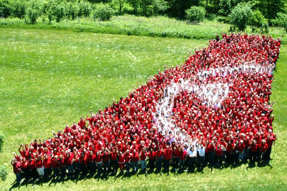 Northwest employees dressed in red and white shirts pose in an open grassy field to form the image of a NWA tail with the final 